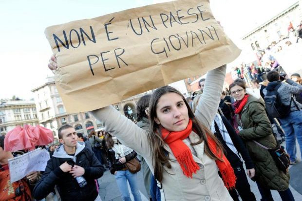 Giovani durante una manifestazione con uno striscione con la scritta "Non è un Paese per giovani".
