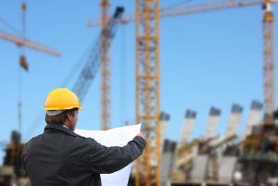 Cantieri: un ingegnere controlla i piani delle costruzioni, sullo sfondo gru.