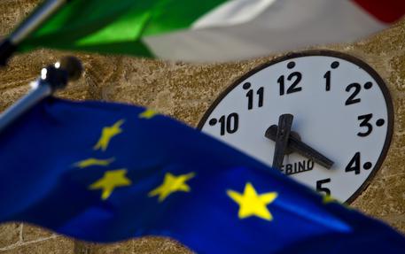Un orologio tra due bandiere, quella Italiana e quella Europea. Manovra