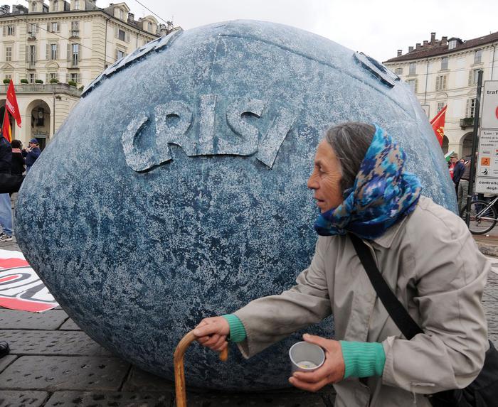 Una donna anziana con un bastone e un bicchiere per l'elemosina pasa davanti ad una sfera con la scritta ''crisi '' a Torino in una foto di archivio. Moody's