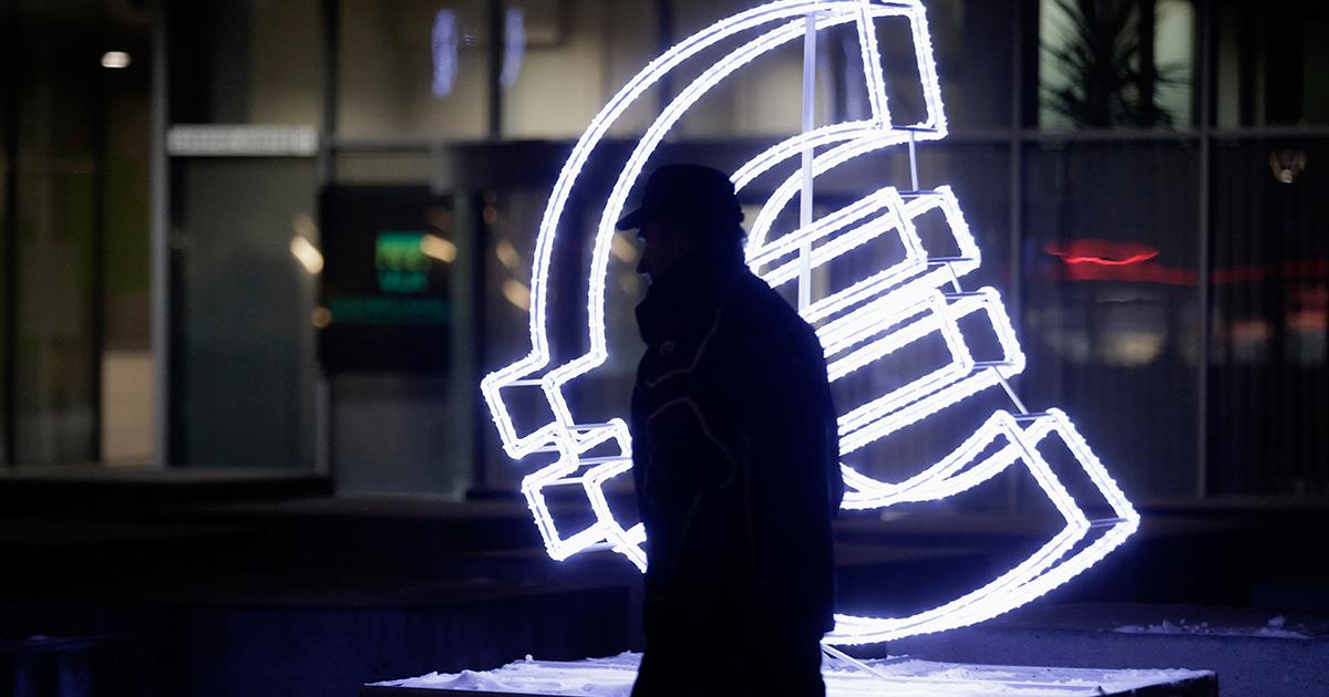 Euro, luci e ombre. Una persona passa davanti al simbolo dell'Euro illuminato.