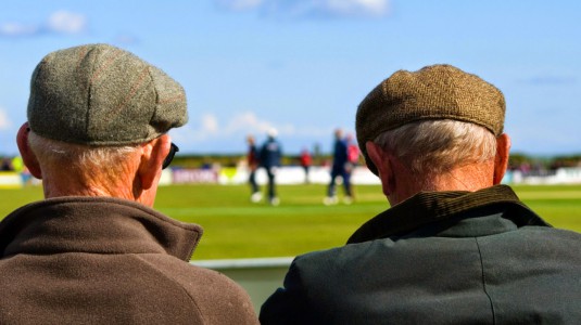 Due pensionati seduti con il berretto in testa, visti di spalle.