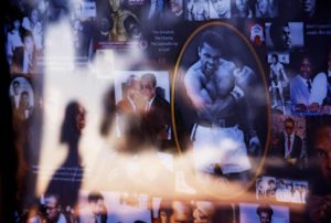 A collage of Muhammad Ali images is displayed as a visitor is reflected in the glass while looking over a makeshift memorial to Ali at the Muhammad Ali Center Thursday, June 9, 2016, in Louisville, Ky.  (ANSA/AP Photo/David Goldman)