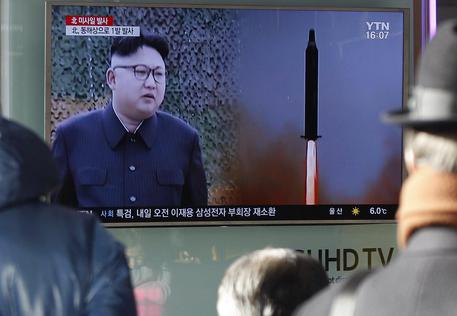 Kim Jong-un durante una conferenza stampa. Alle sue spalle un video con un missile in volo.