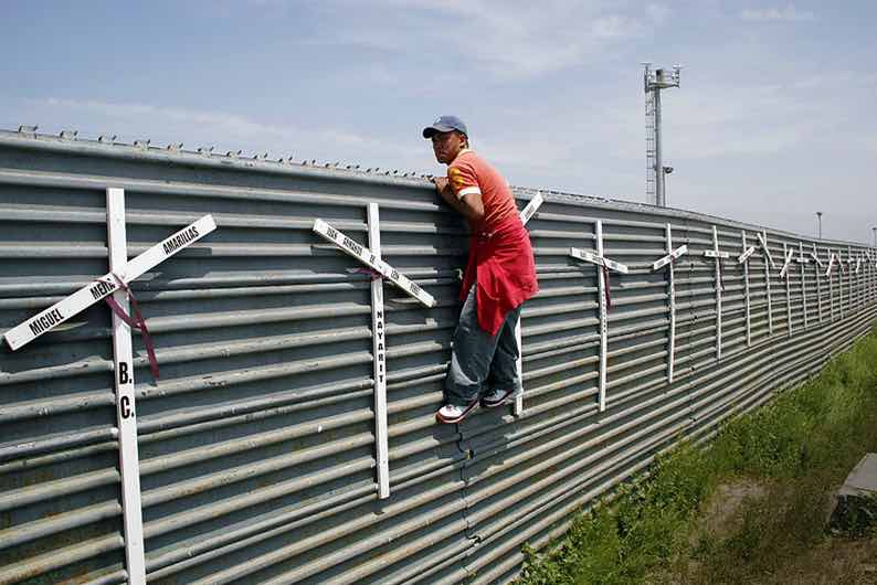 Un messicano cerca di scavalcare il muro tra Messico e Usa con le croci in ricordo dei morti nel tentativo.