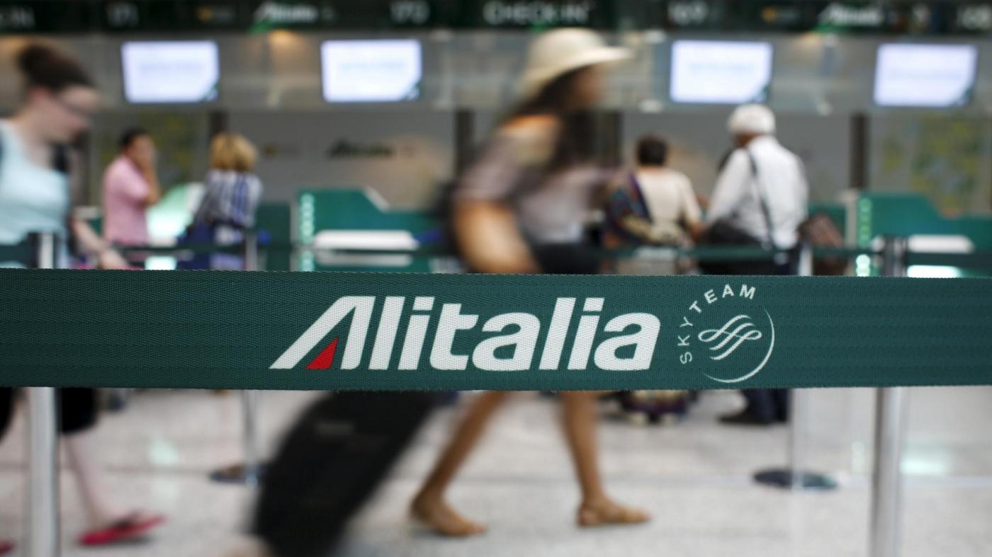 Un passeggero in transito davanti una porta in vetro con la scritta Alitalia