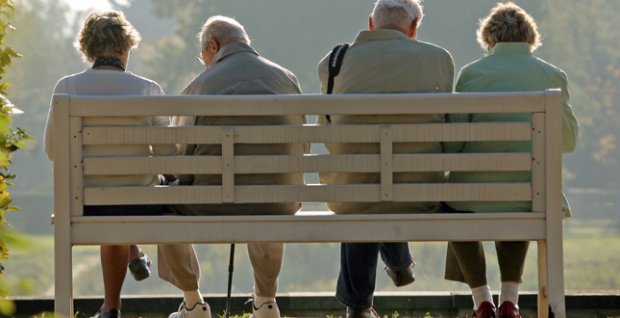 Due coppie di pensionati seduti in panchina, ripresi di spalle.