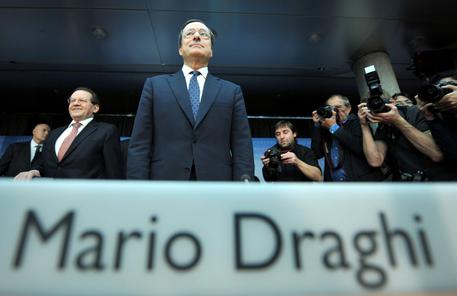 Mario Draghi su un palco con su scritto il suo nome.