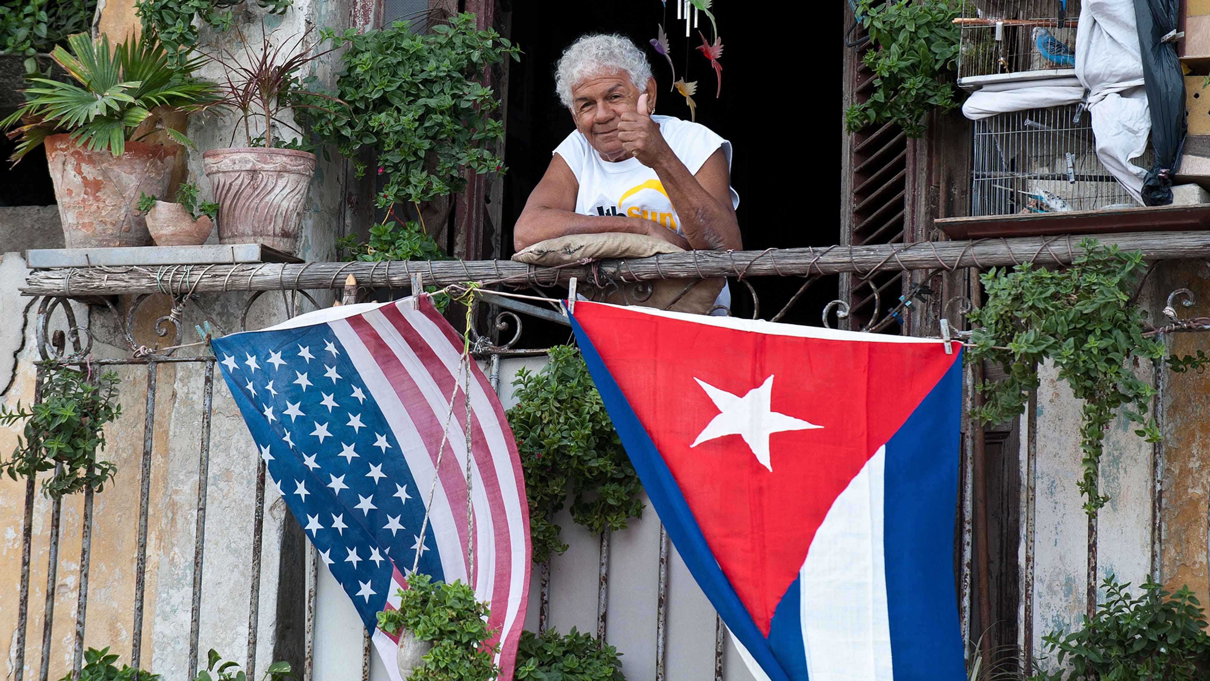 L'Avana: donna sul balcone di casa con le bandiere di Cuba e Stati Uniti.