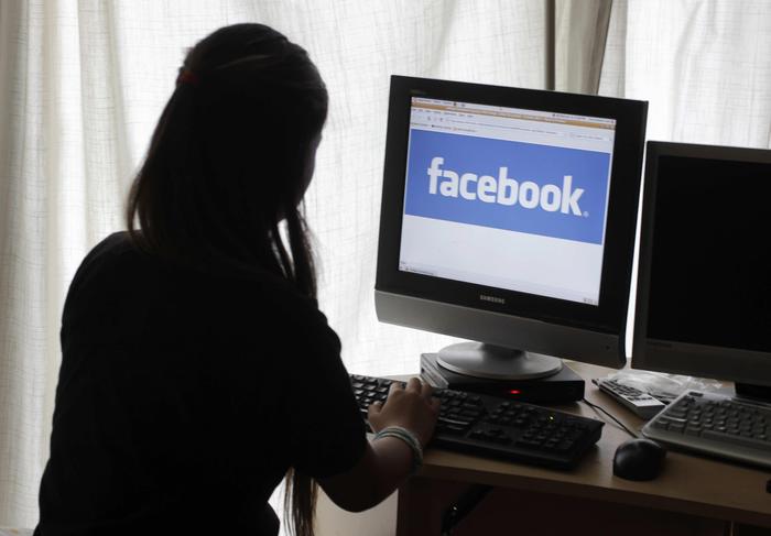 Ragazza seduta davanti al computer seguendo Facebook.