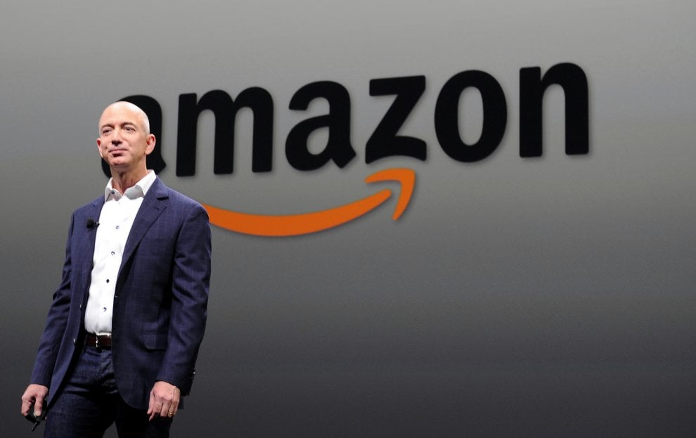Jeff Bezos in primo piano, dietro il simbolo di Amazon