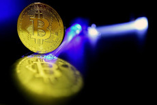 Una moneta di bitcoin riflessa sun tavolo di vetro colpita da un raggio di luce viola.