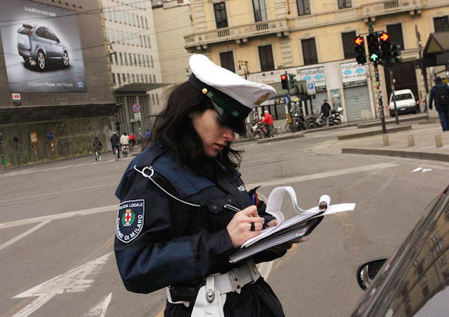 Nella foto una vigile urbano mentre multa un'auto in sosta vietata.