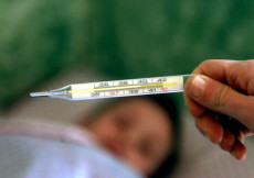 Un termometro per misurare la febbre in primo piano, un bambino a letto in secondo piano.
