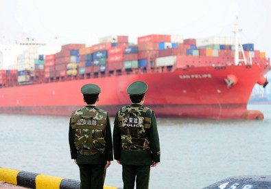 Due militari cinesi osservano una nave container entrare in porto. Cina