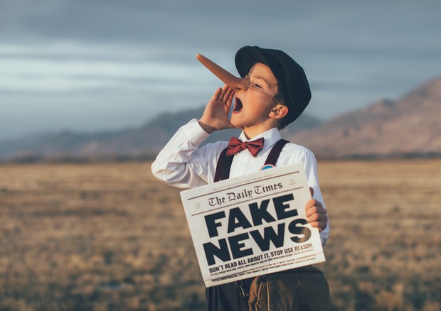 Un bambino col naso di Pinocchio e un giornale dove spicca la frase "Fake news"