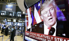 Schermo gigante con l'immagine del presidente Donald Trump annunciando le riforme economiche, sullo sfondo schermi con i valori della borsa.