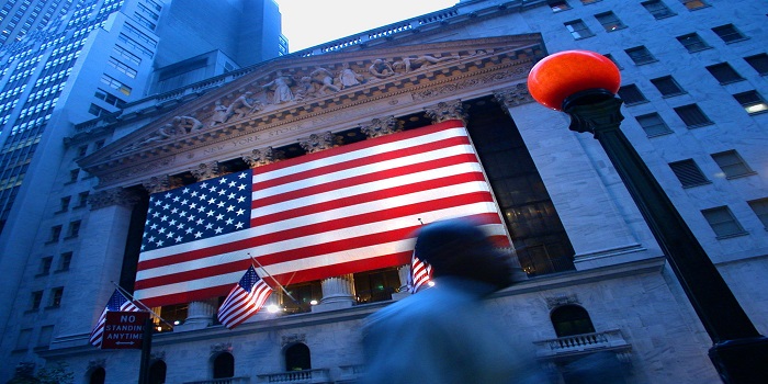 Una persona cammina in Wall Street, sede della borsa di NY, con la bandiera americana.