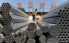 Tubi di acciaio accatastati in Cina ed un operaio al lavoro.
