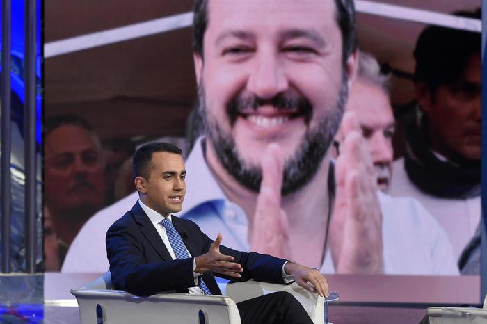 Di Maio seduto in poltrona, sullo sfondo Salvini.