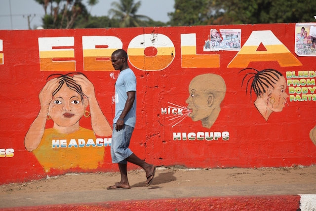 Una persona cammina davanti ad un muro con un graffiti di immagini di ebola