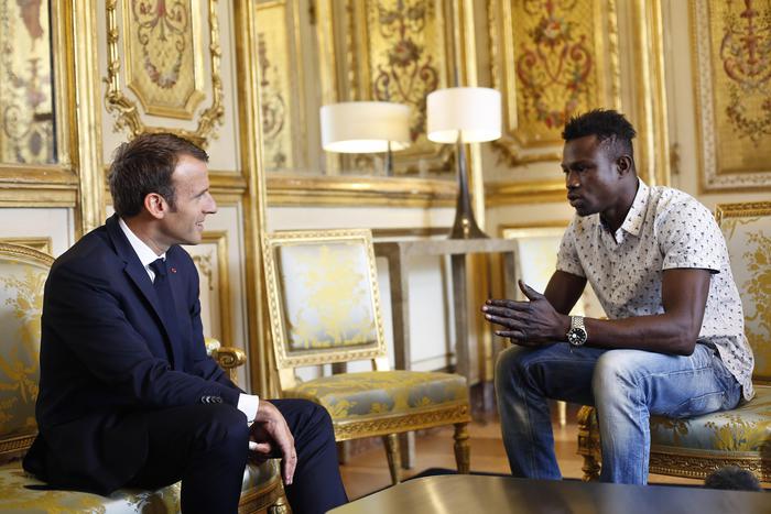 A destra Mamoudou Gassama, a destra Emmanuel Macron all'Eliseo, seduti nelle poltrone mentre conversano.