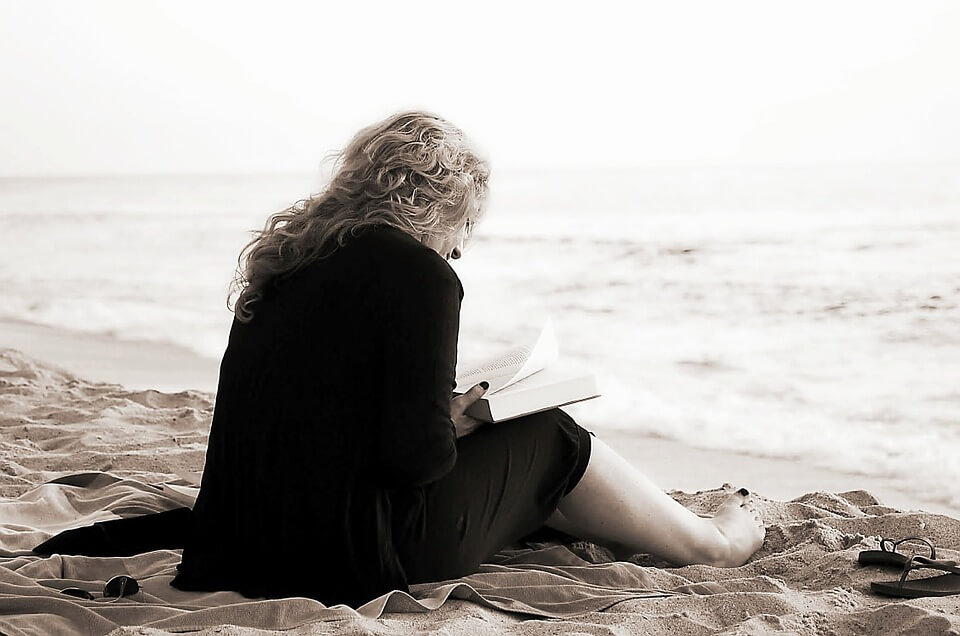 Donna di mezz'età seduta di spalle sulla riva del mare