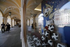 Persone passeggiano in una via di San Pietroburgo con la vetrina di un negozi con palloni e mascotte del mondiale.