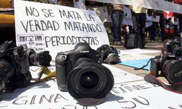Macchina fotografica appoggiata a terra su un manifesto di protesta contro l'assassinio di giornalisti. Honduras