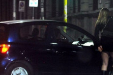 Un'auto si avvicina a una prostituta in strada di notte.