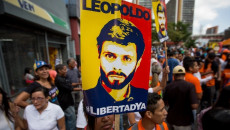 In primo piano un manifesto con l'immagine di Leopoldo Lòpez durante una manifestazione