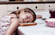Bambina addormentata mentre fa colazione con la faccia sulla fetta di pane.