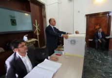Un seggio elettorale durante le votazioni comunali: uno scrutatore al tavolo e il presidente vicino all'urna.