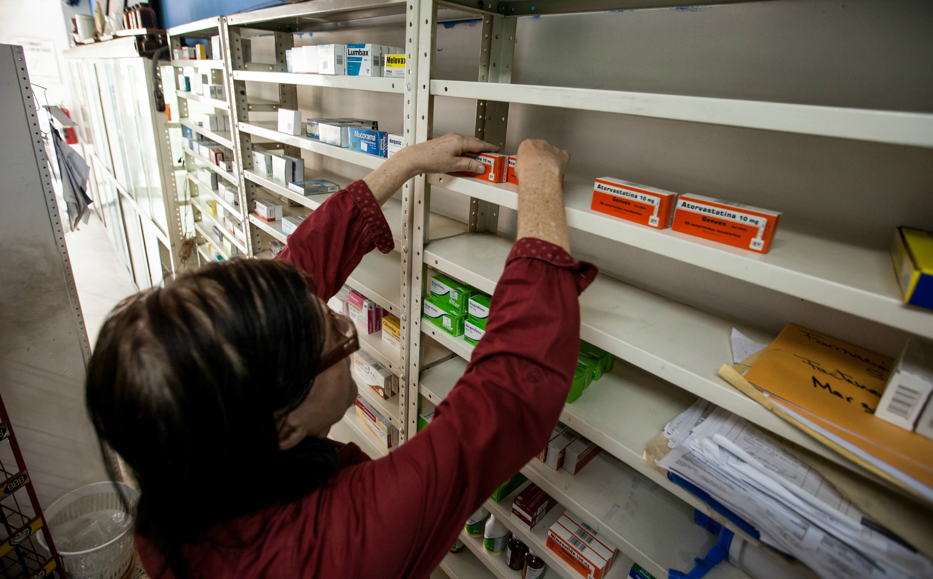 Una mujer buscando medicinas en un estante de Farmacia