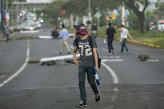 Un ragazzo protesta in strada con il viso coperto da un fazzoletto.