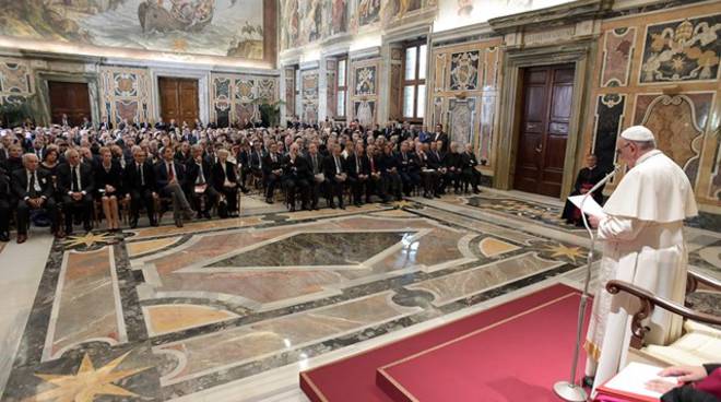 Papa Francesco si rivolge a un gruppo di giornalisti seduti di fronte.