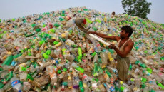 Un indiano spala una montagna di bottiglie di plastica.