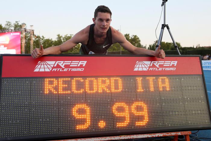 Filippo Tortu festeggia il nuovo record sui 100 metri appoggiato al tabellone con l'indicazione del suo record.