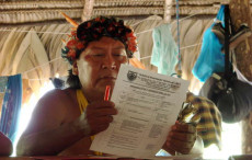 Un capo tribù Yanomami leggendo un modulo ministeriale da compilare.