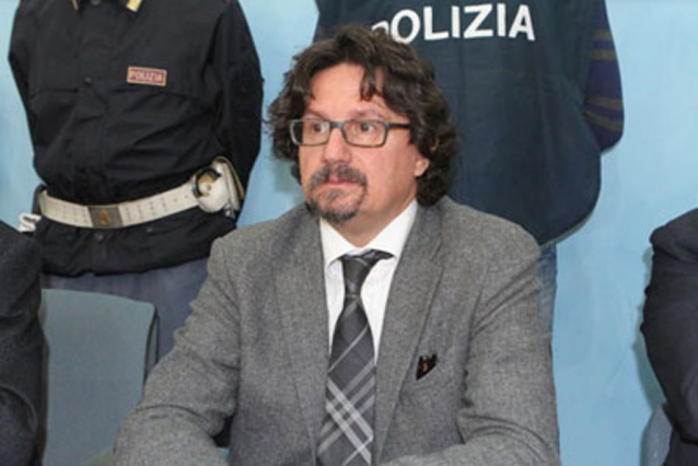Il procuratore di Reggio Calabria Giovanni Bombardieri seduto ad un tavolo, dietro due poliziotti.