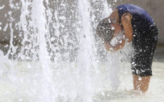 Una persona si rinfresca sotto il getto di una fontana