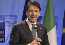 Primo piano del primo Ministro, Giuseppe Conte. Alle sue spalle la bandiera italiana e quella europea.