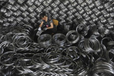 Un lavoratore dello stabilimento di lavorazione dell'acciaio a Hangzhou, circondato da bobine di acciaio. Cina
