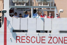 La fiancata della Diciotti con la scritta "Rescue Zone" e i migranti appoggiati a paratia.