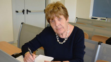 Nella foto Rosella Morbidelli, 73 anni, seduta ad un banco con la penna in mano ed un blocco di appunti.