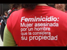 Una donna di spalle con una camicia con la scritta : Femminicidio: mure asesinada por un hombre que la considera de su propiedad"