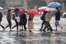 Persone per strada con gli ombrelli aperti per ripararsi dall'abbondante pioggia.