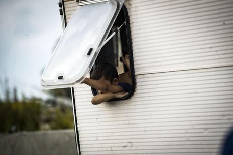 Particolare di un bambino affacciato dalla finestra di una roulotte di un campo nomadi.
