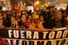Manifestanti per strada con uno striscione con la scritta "Fuera todos los corruptos"