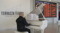 Vista della Terrazza Termini a Roma, un musicista suona il piano e sullo sfondo il tabellone degli orari